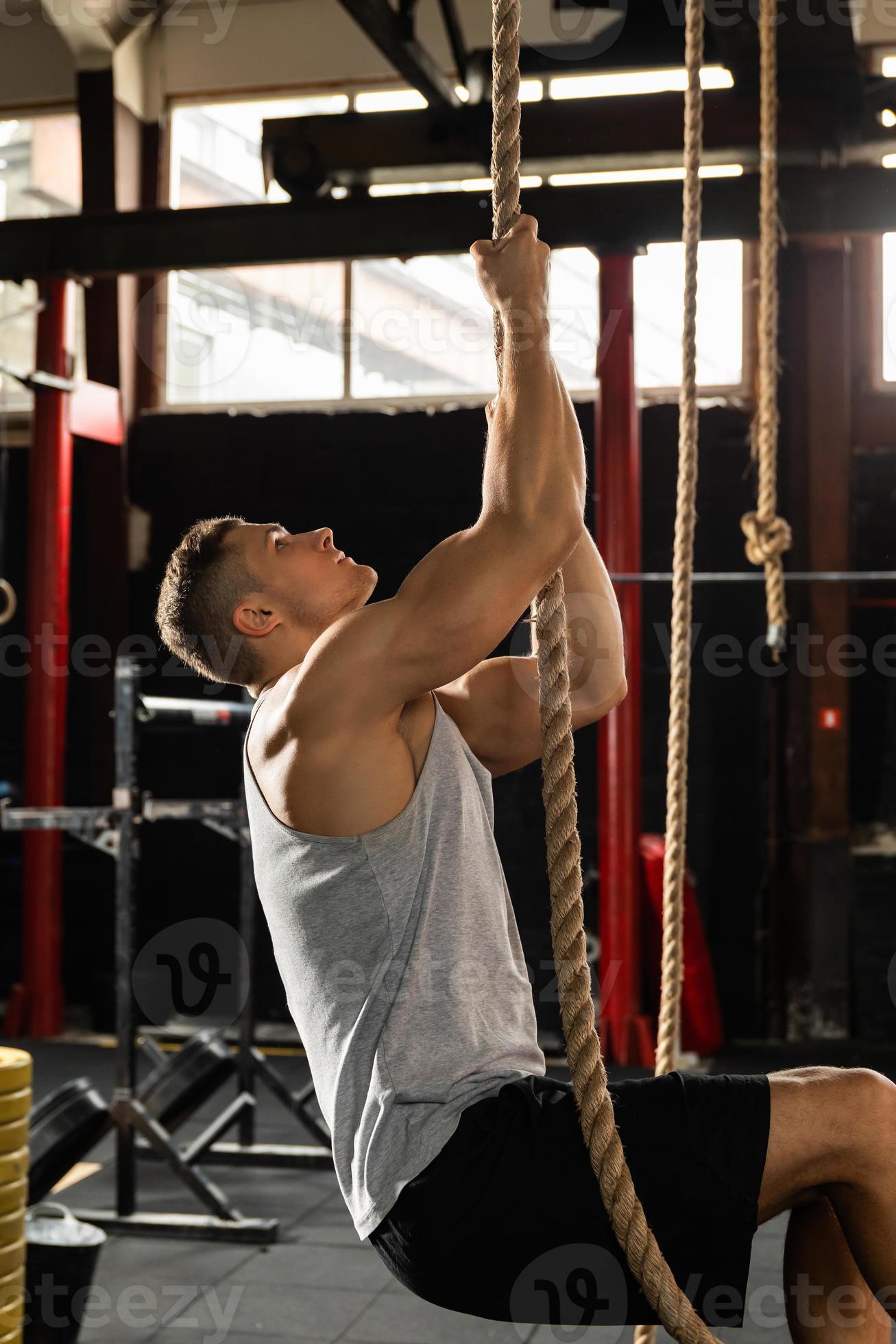 Sportsman doing rope climbing exercise in cross training gym