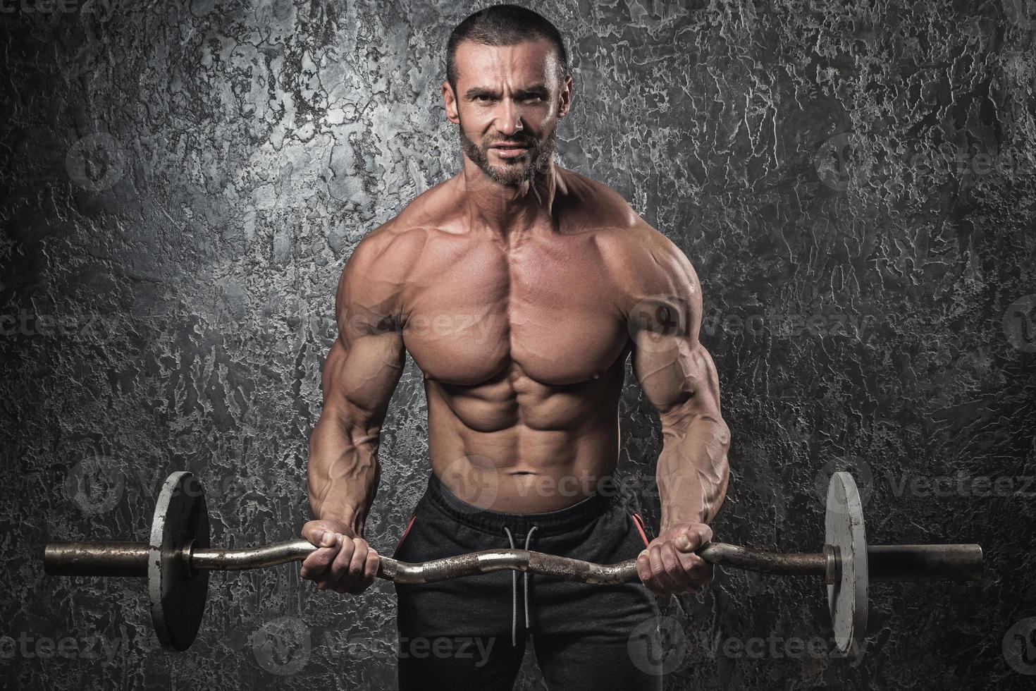 Bodybuilder man with barbell against concrete wall photo