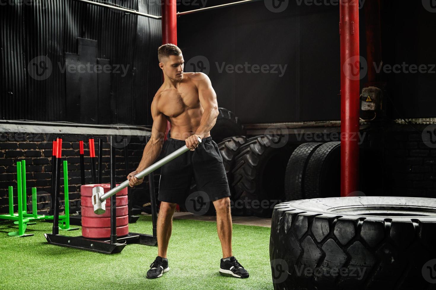 Man is hitting tire with a sledgehammer during his cross training workout photo