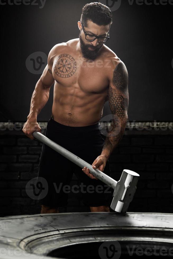 Man is hitting tire with a sledgehammer during his cross training workout photo