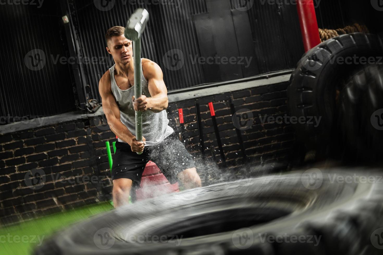 Man is hitting tire with a sledgehammer during his cross training workout photo