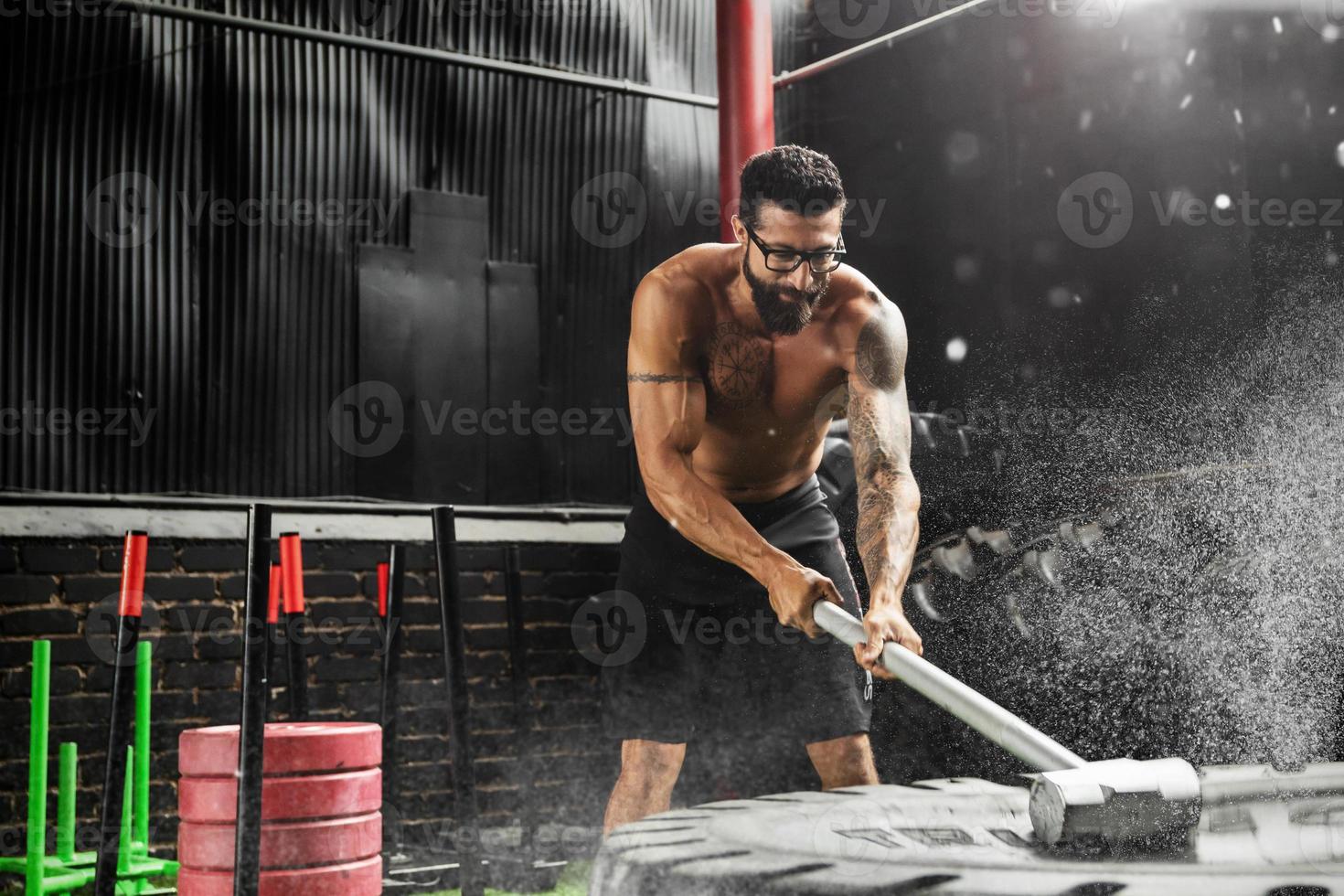 Man is hitting tire with a sledgehammer during his cross training workout photo