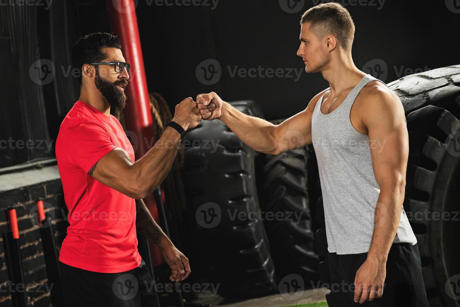 Two muscular men are making fist bump gesture during workout in the gym photo