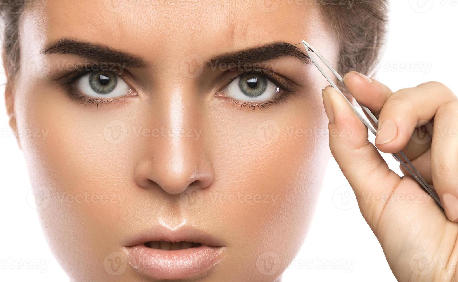 Close-up of female face and eyebrow with tweezers photo