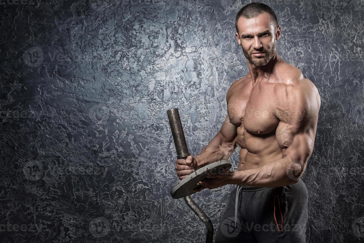 Bodybuilder man with barbell against concrete wall photo