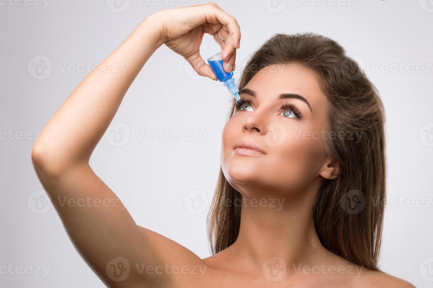 Studio shot of beautiful woman using eye drops photo