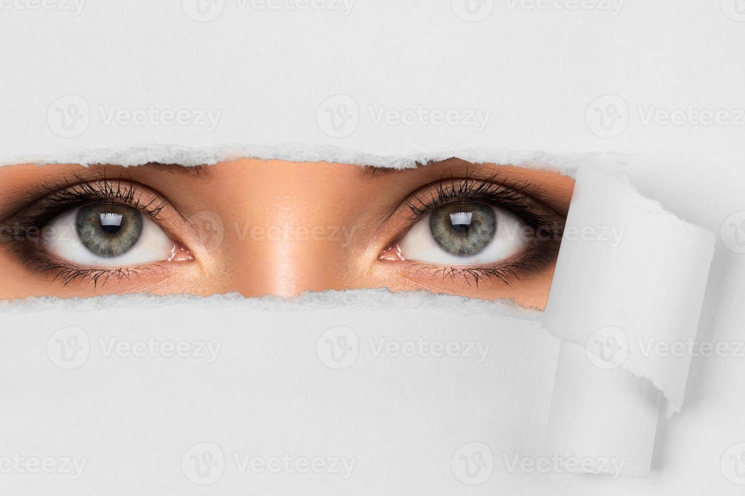 Young female eyes looking through torn paper photo