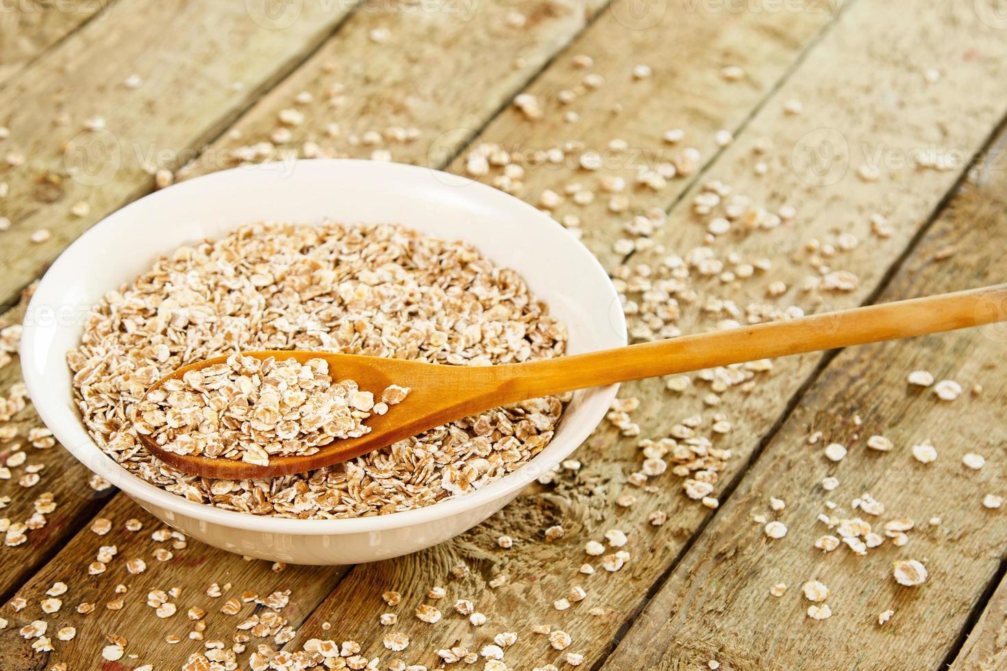 Uncooked oatmeal, white bowl and wooden spoon on the table photo