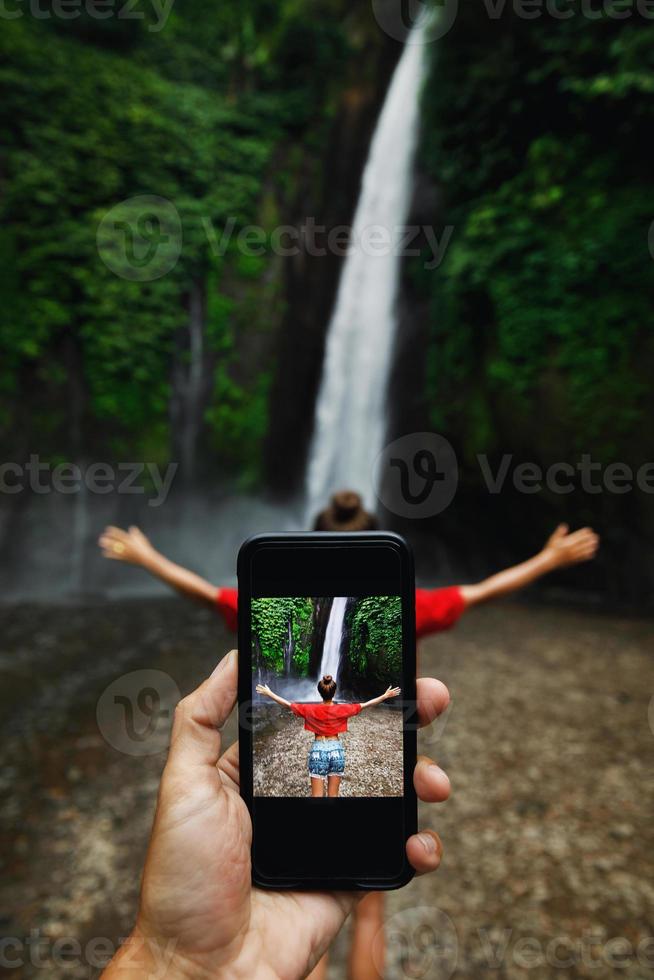 Man taking picture of her girlfriend beside beautiful waterfall photo