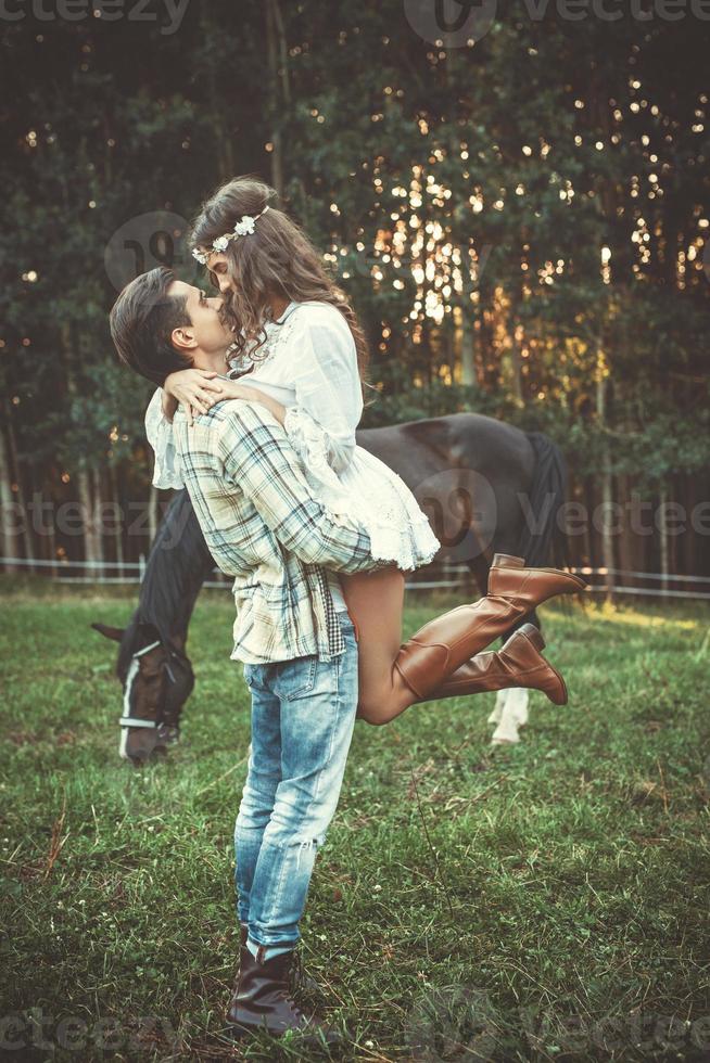 pareja joven en abrazo en el prado con caballos foto