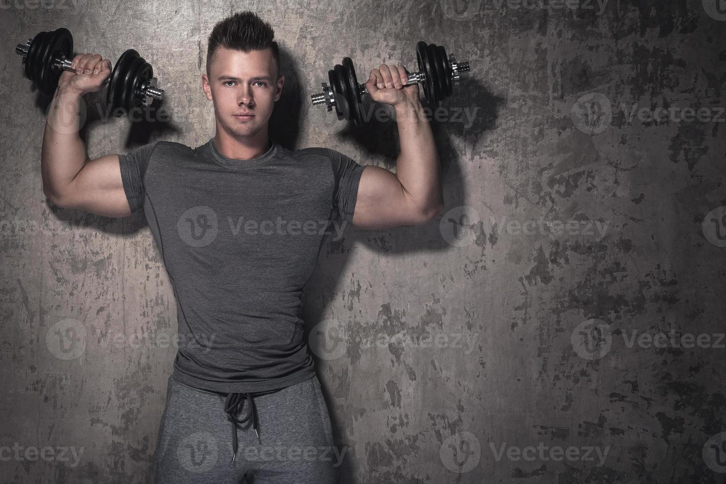 Young bodybuilder is doing overhead press exercise photo