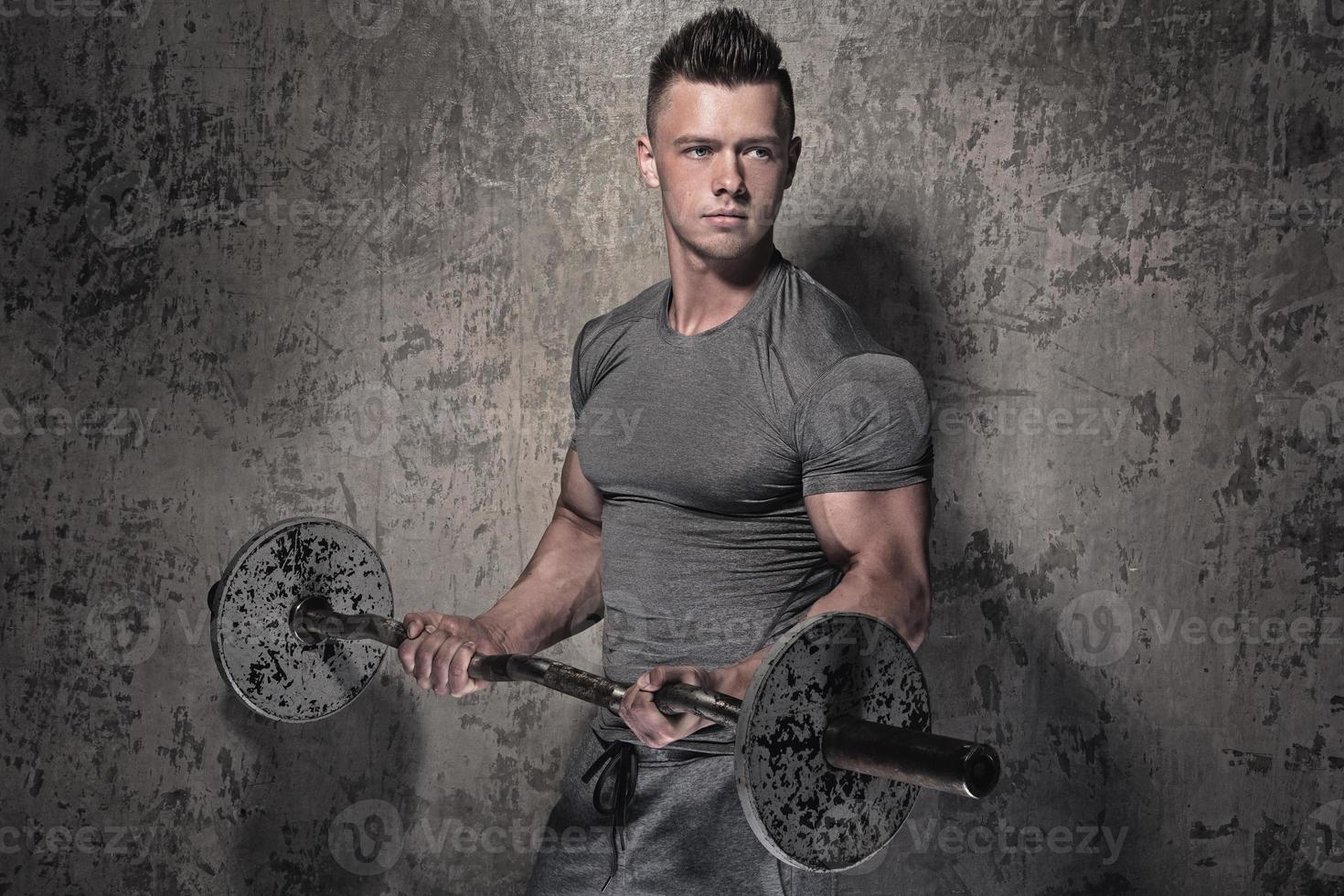 Young bodybuilder with barbell in against cocnrete wall photo