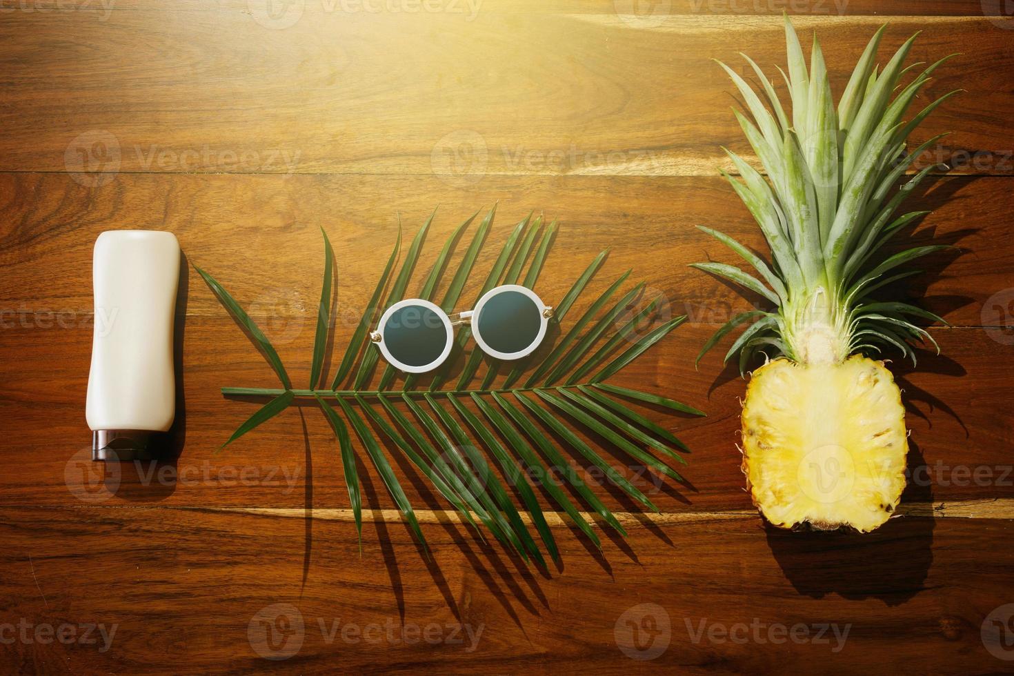 Flat lay of Sunscreen, sunglasses and pineapple fruit photo