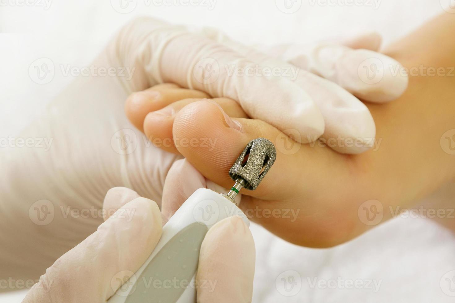 Pedicure master work. Closeup of female feet and hands in gloves with a special machine tool. photo