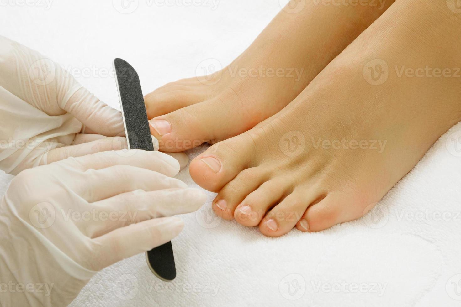 Pedicure master work. Closeup of female feet and hands in gloves with a nail file. photo