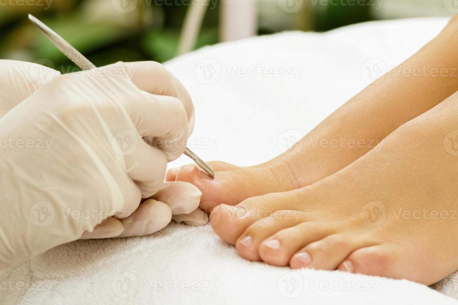 Pedicure master work. Closeup of female nails and hands in gloves with a special steel tool. photo