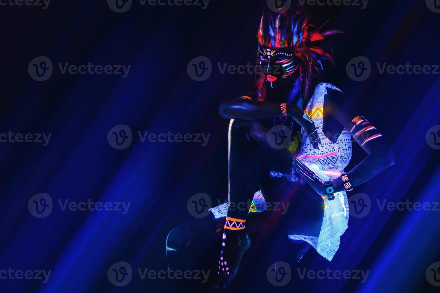 Model in image of Native american with neon makeup, which made of fluorescent paint in ultraviolet light. photo