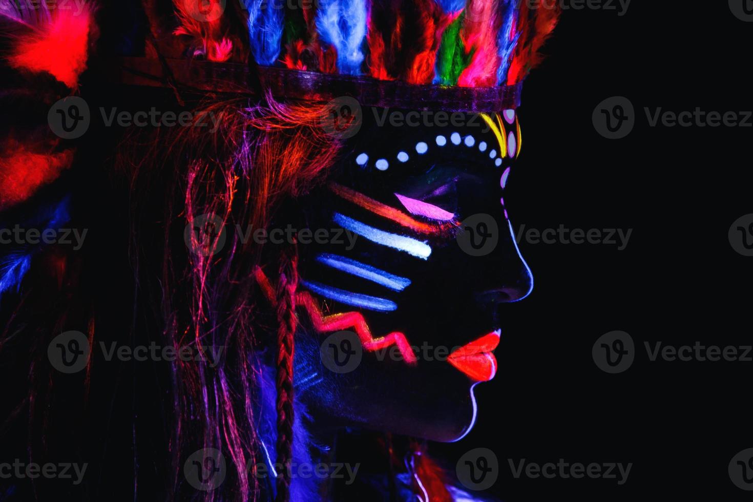 Model in image of Native american with neon makeup, which made of fluorescent paint in ultraviolet light. photo