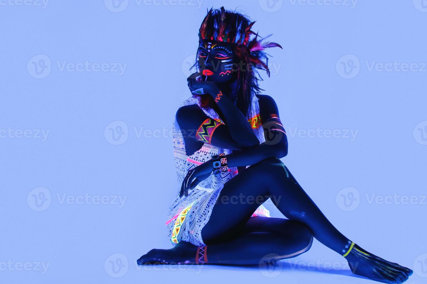 Model in image of Native american with neon makeup, which made of fluorescent paint in ultraviolet light. photo