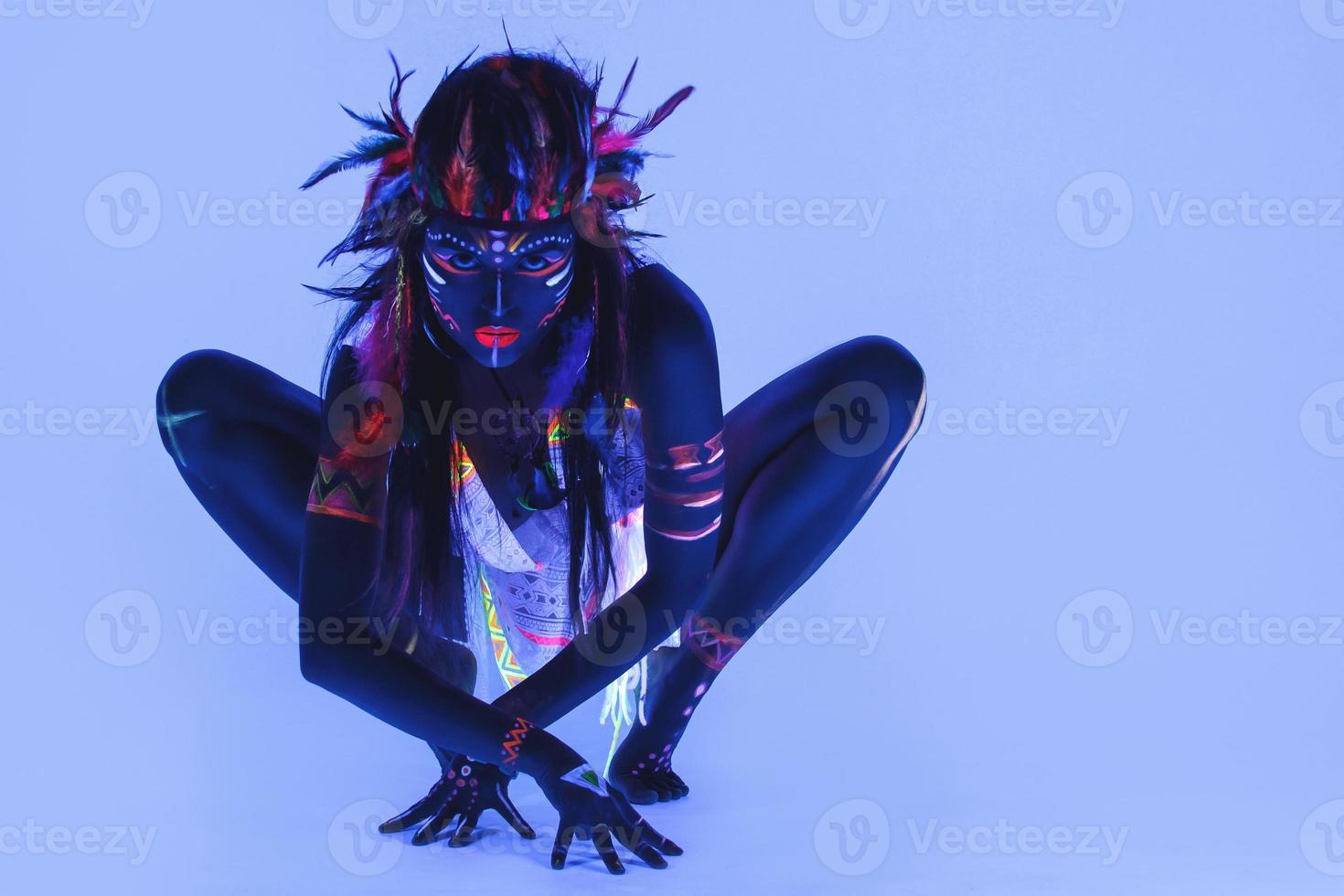 Model in image of Native american with neon makeup, which made of fluorescent paint in ultraviolet light. photo