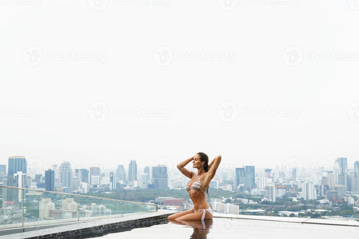 Woman relaxing on a rooftop pool with a beautiful city view photo