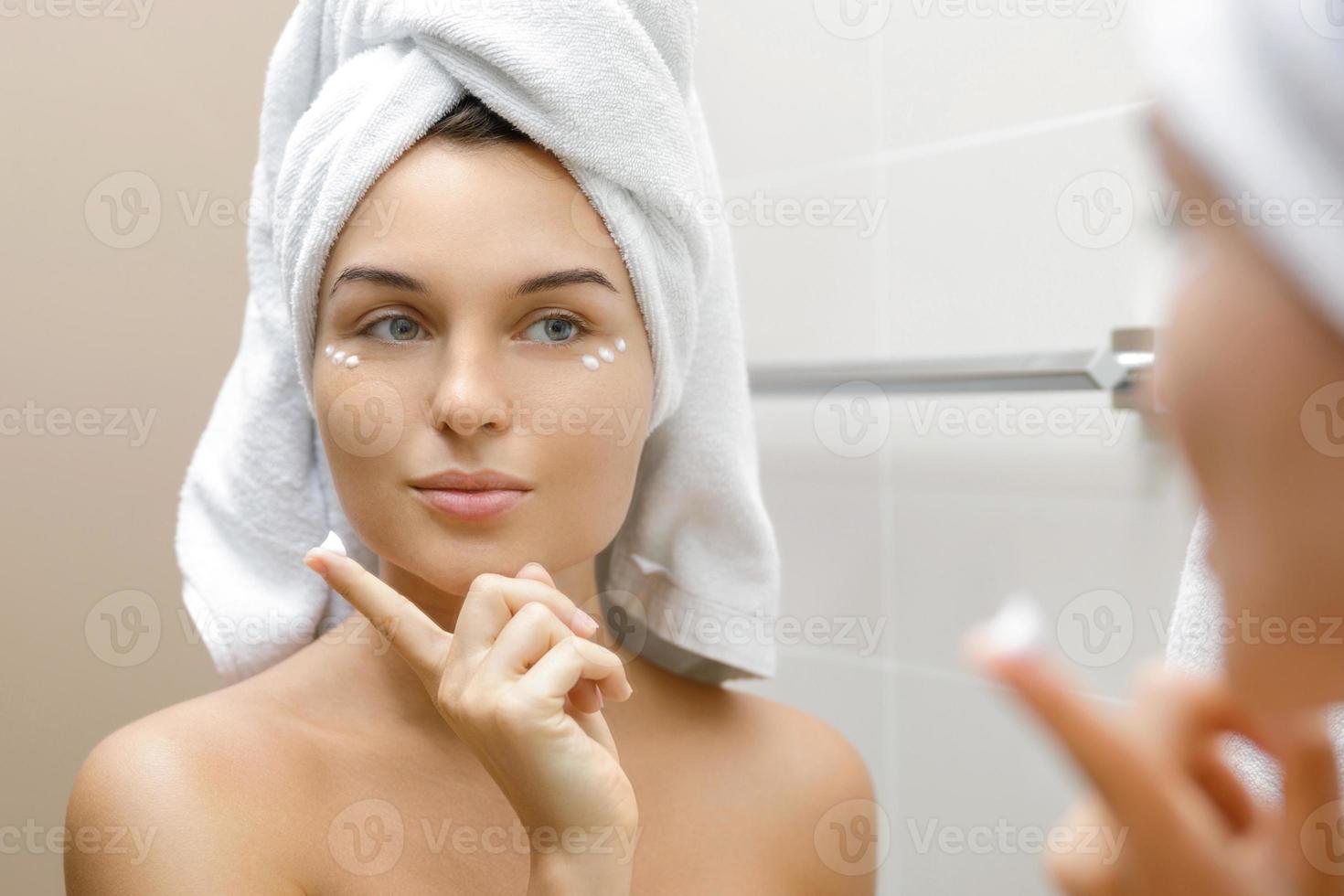 Woman using moisturizing and anti-aging cream under her eyes photo