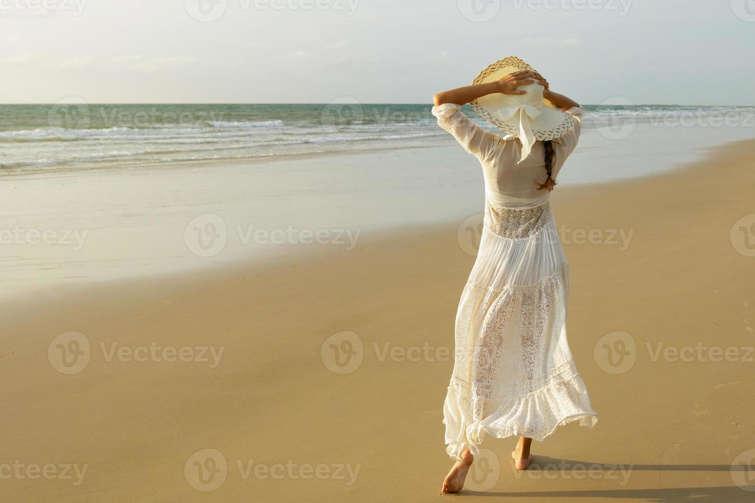 Woman wearing beautiful white dress is walking on the beach during sunset photo