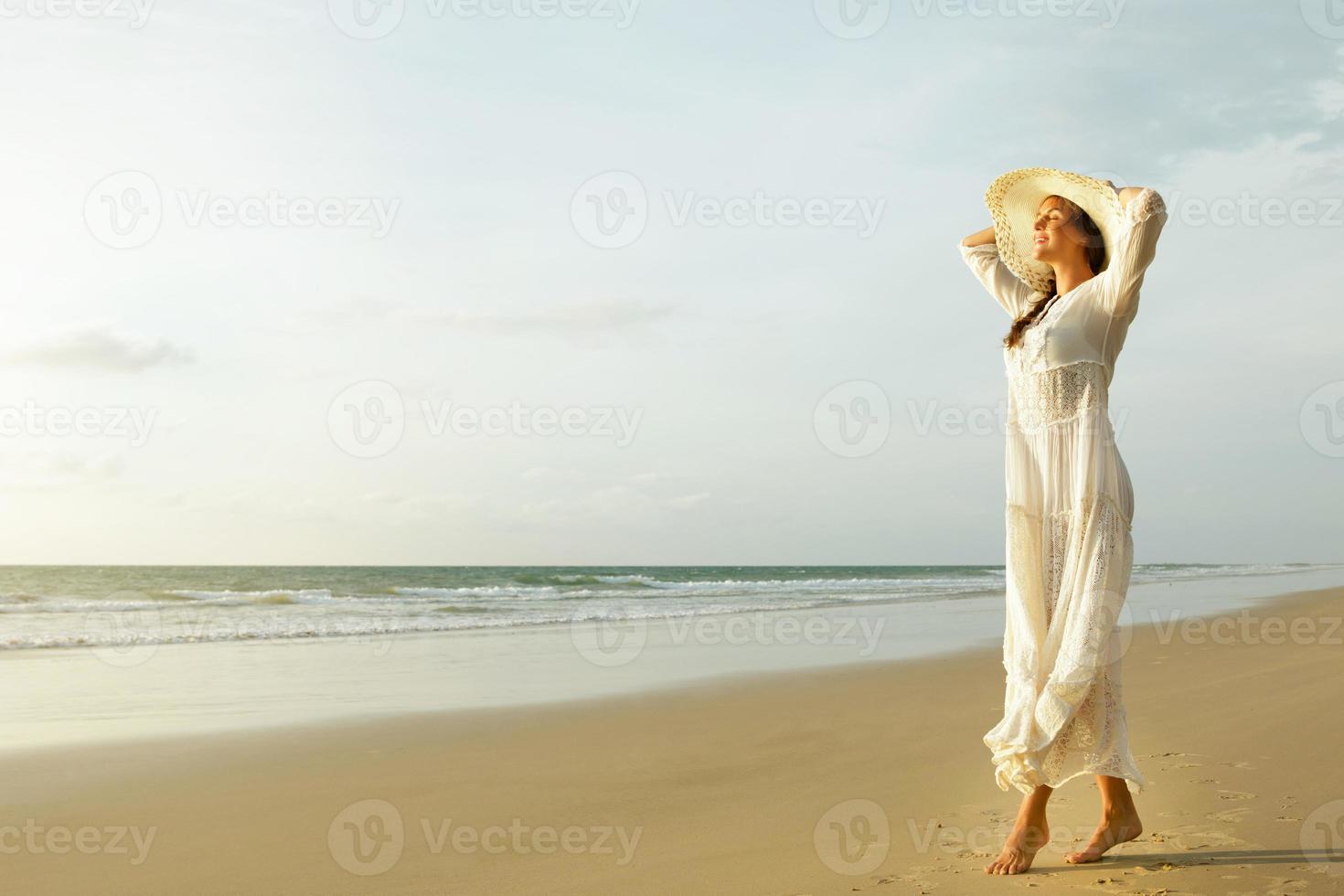 Woman wearing beautiful white dress is walking on the beach during sunset photo