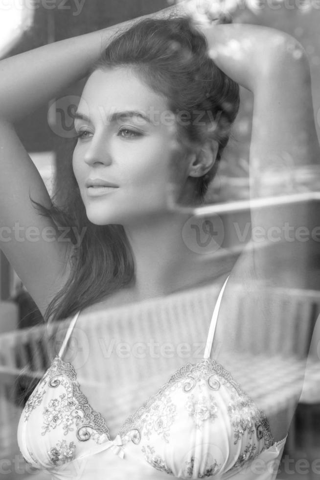 Beautiful young woman is looking through the window glass photo