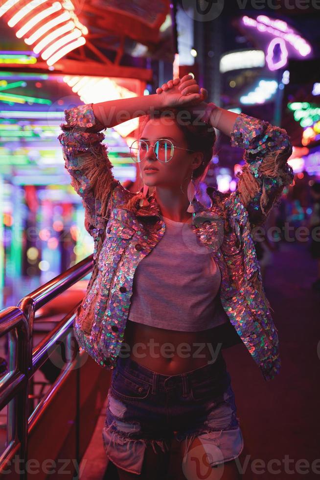 Woman wearing sparkling jacket on the city street with neon lights photo