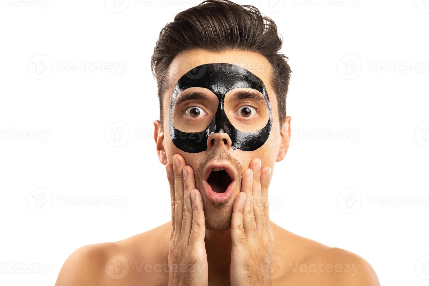 Young guy with a black charcoal mask on his face on white background. photo