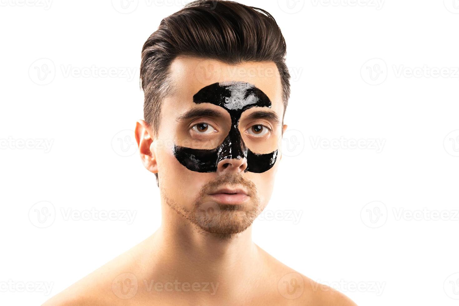 Young guy with a black charcoal mask on his face on white background. photo