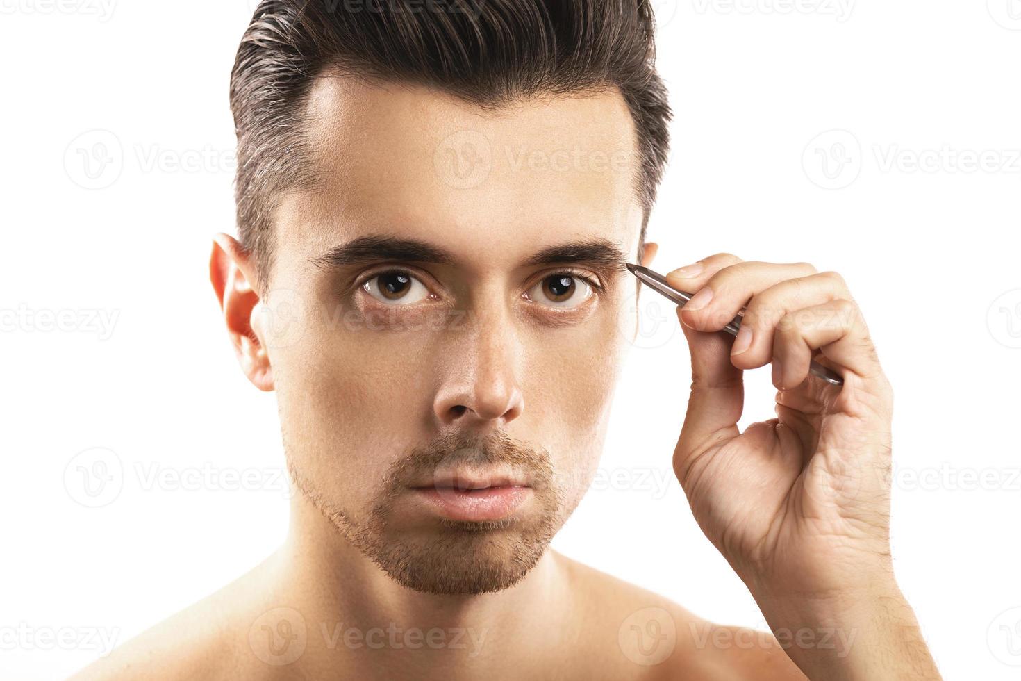 Young guy holding tweezers near his eyebrow for that's shape correction photo