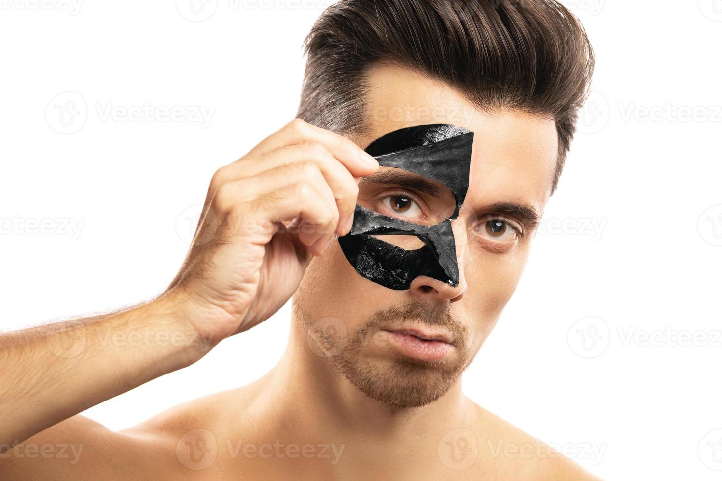 Young guy with a black charcoal mask on his face on white background. photo
