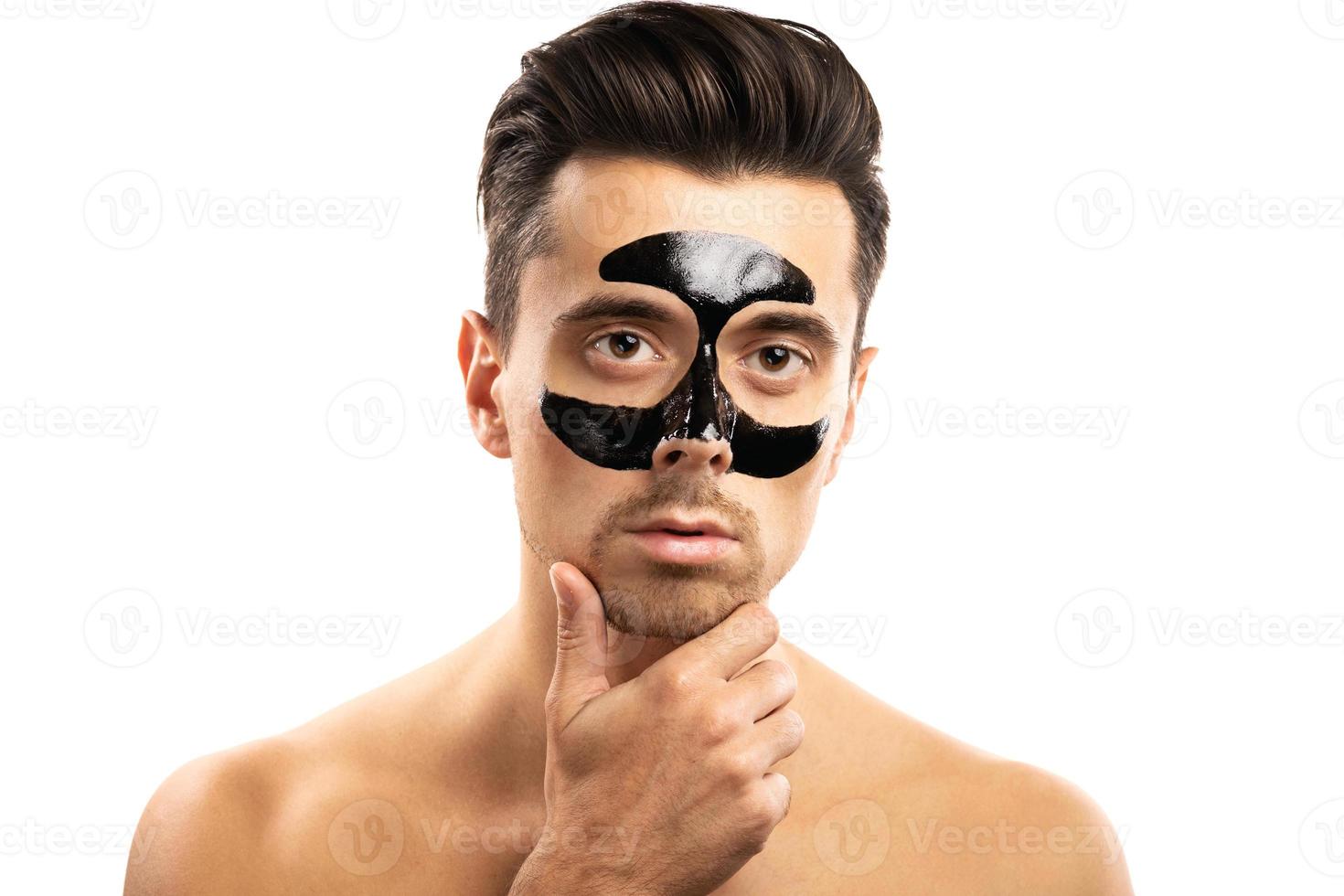 Young guy with a black charcoal mask on his face on white background. photo