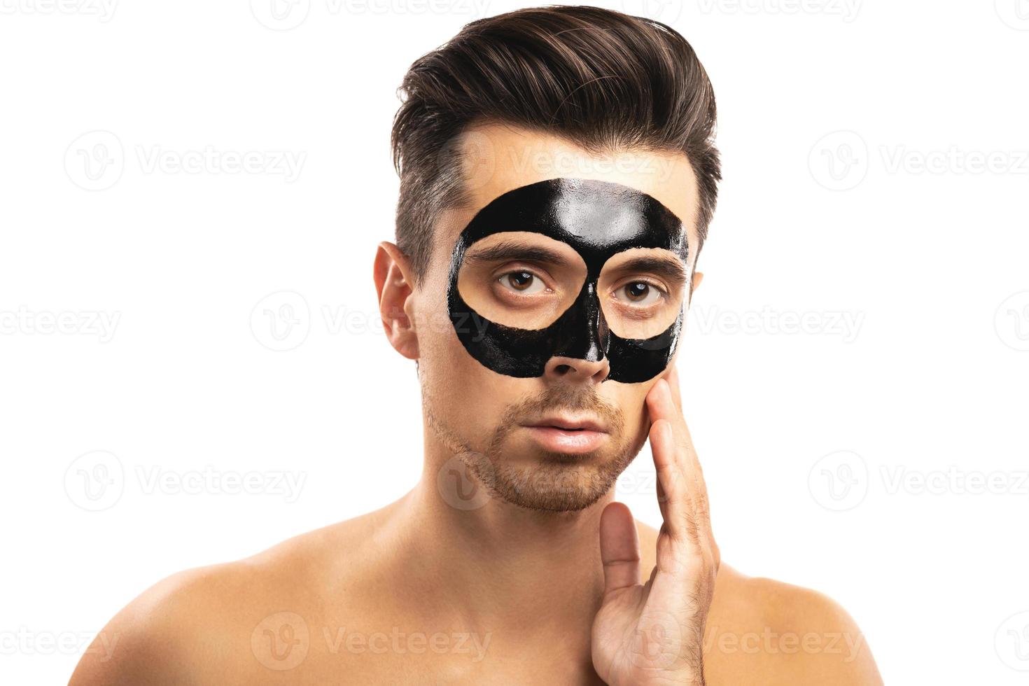 Young guy with a black charcoal mask on his face on white background. photo