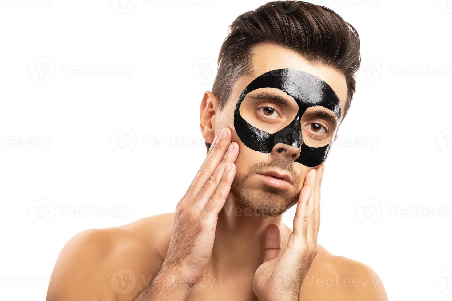 Young guy with a black charcoal mask on his face on white background. photo