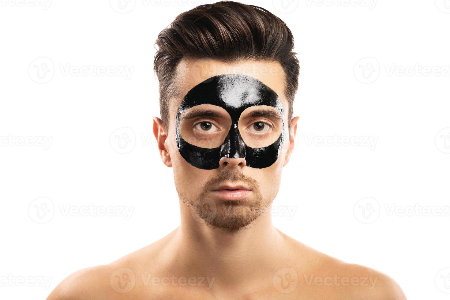 Young guy with a black charcoal mask on his face on white background. photo