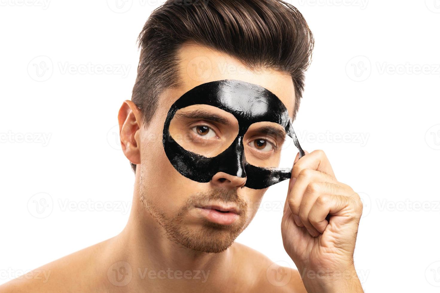 Young guy with a black charcoal mask on his face on white background. photo