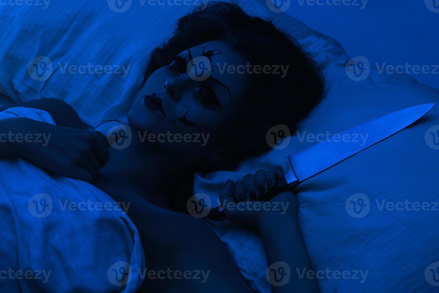 Spooky porcelain speaking doll holding knife and lying in the bed photo