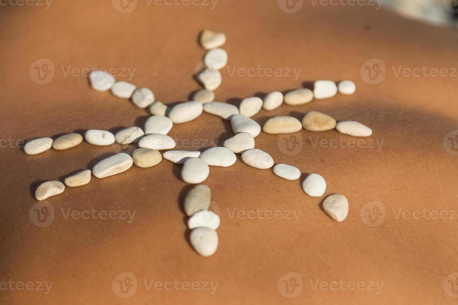 sol hecho de piedras de guijarros en la espalda femenina foto