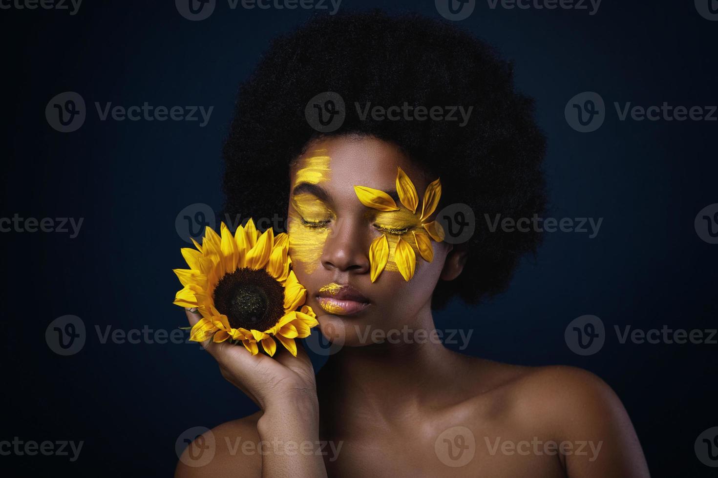 mujer africana con un girasol y maquillaje creativo en la cara foto