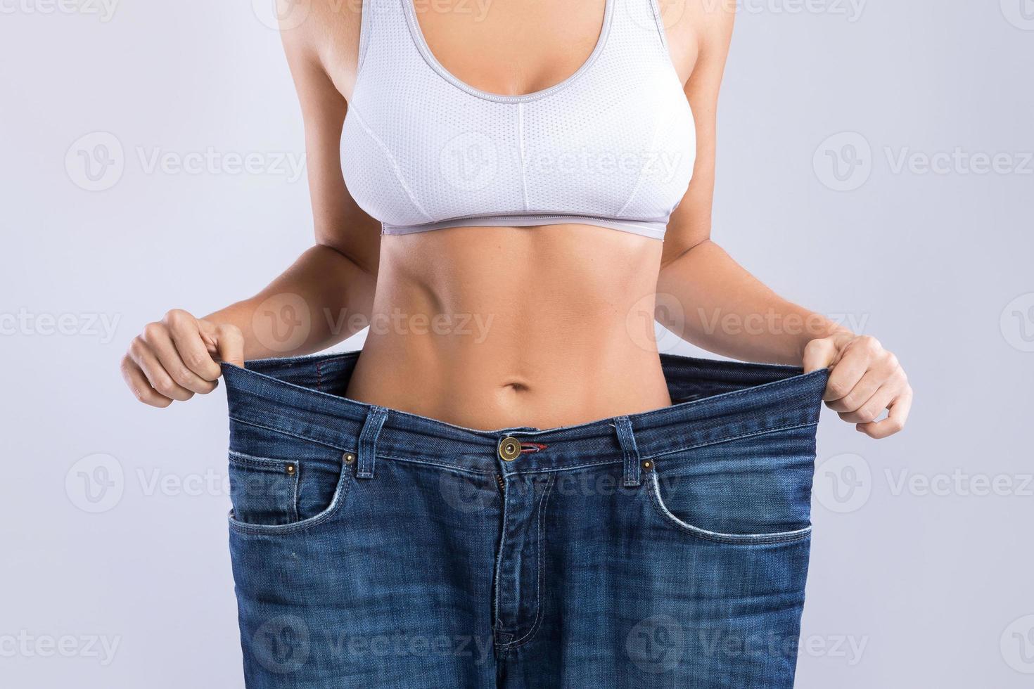 mujer feliz usando jeans después de la pérdida de peso sobre fondo gris foto