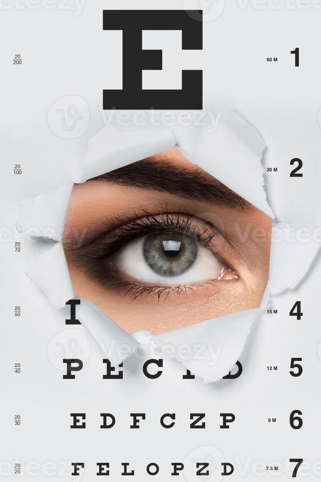 Woman looking throug torned papaer with eye chart photo