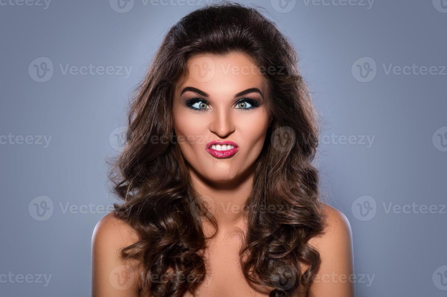 Young woman making silly facial expression on gray background photo