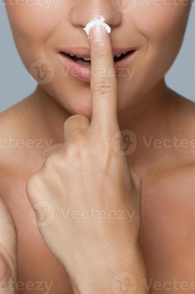 Woman is applying cream on her nose photo