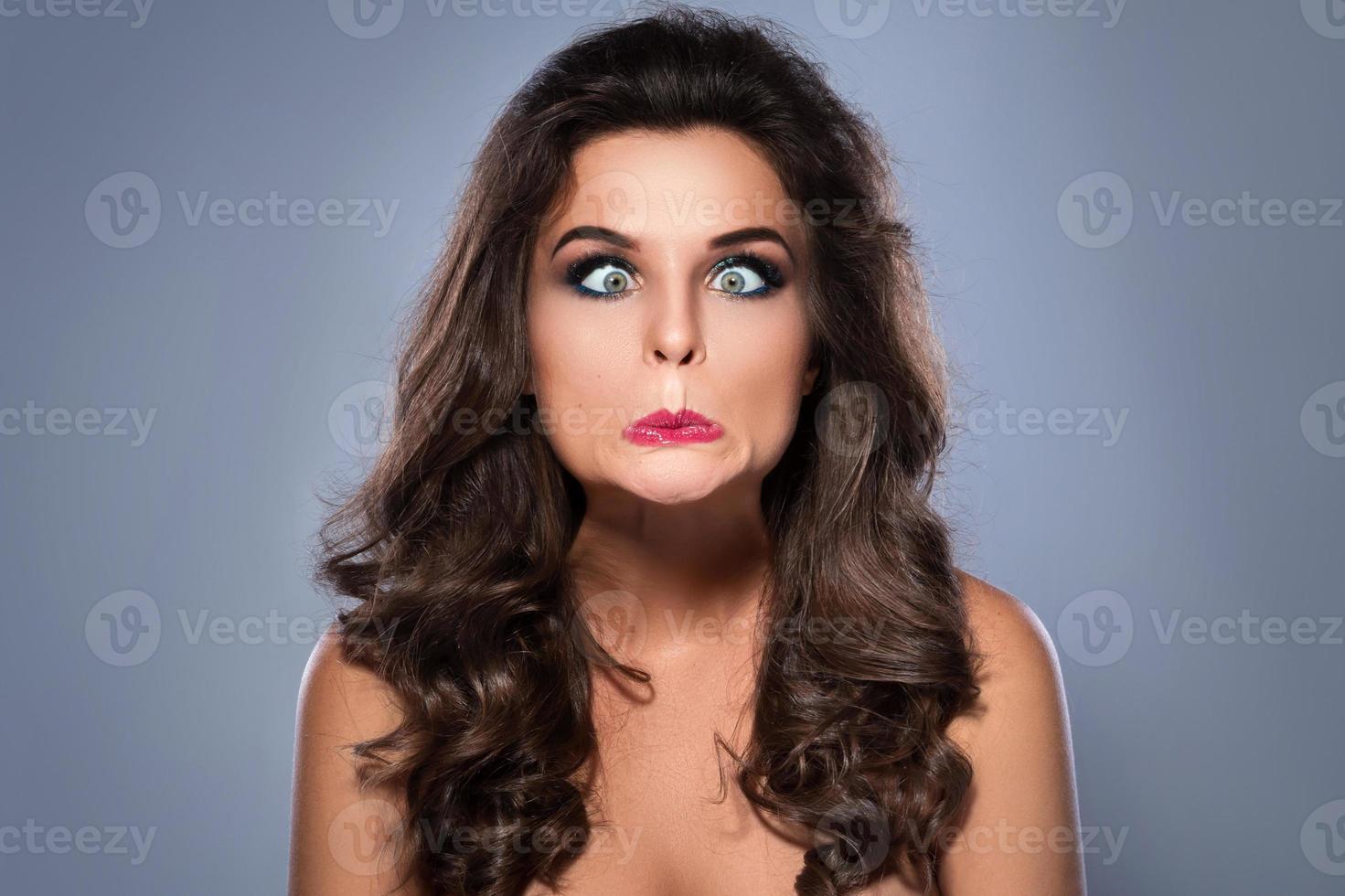 Young woman making silly facial expression on gray background photo