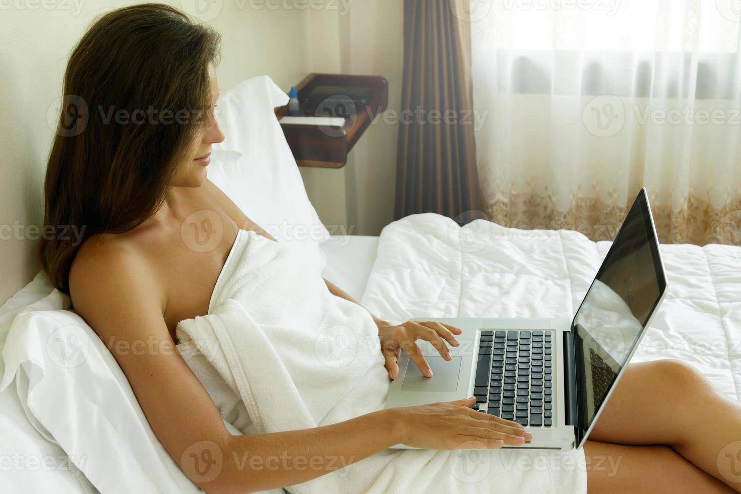 Woman lying on the bed and using laptop pc photo