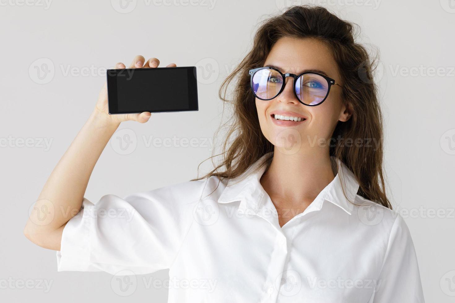 mujer de negocios que muestra la pantalla del teléfono inteligente sobre fondo gris foto