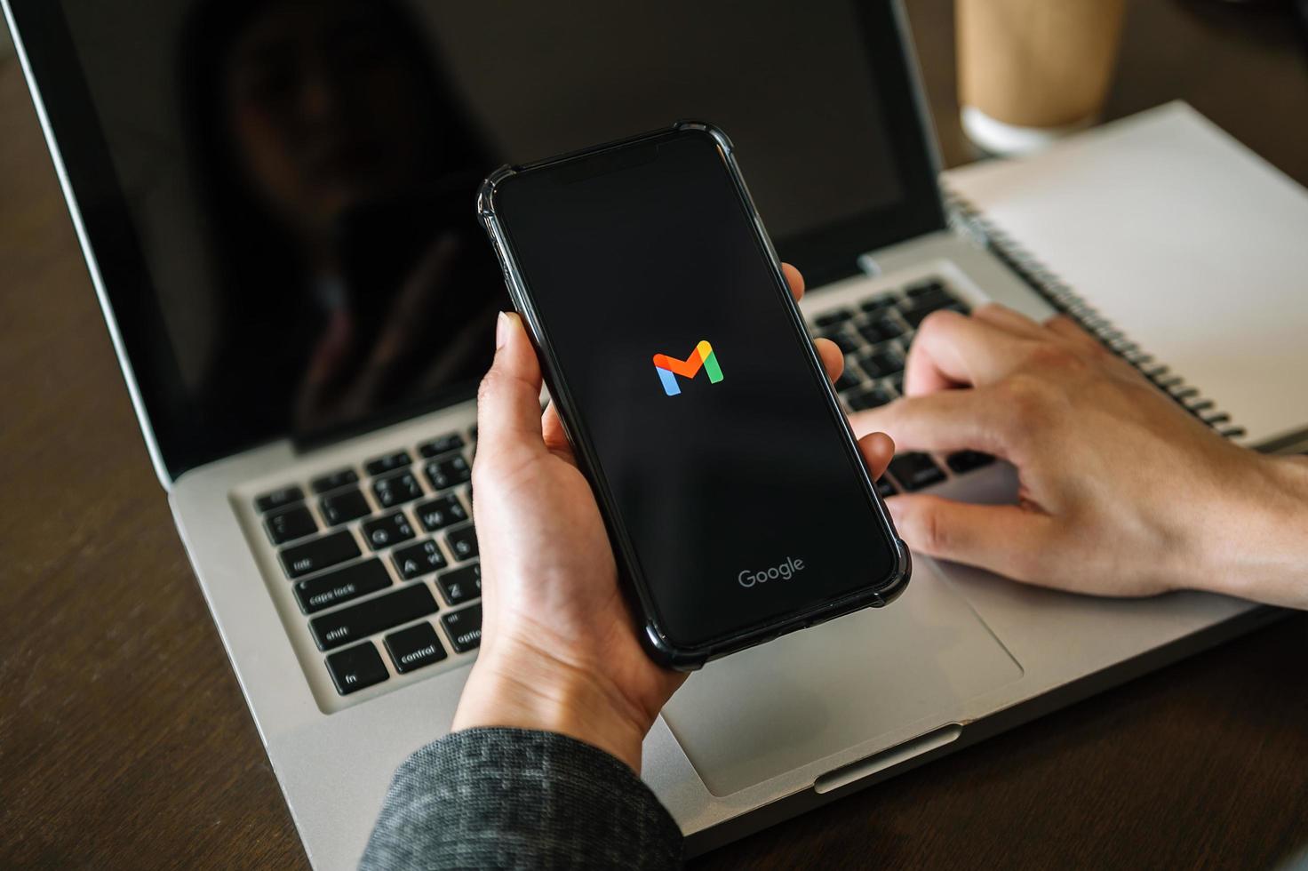 hand holding a smartphone with Gmail app on the screen with a computer beside it. Wooden Background. photo